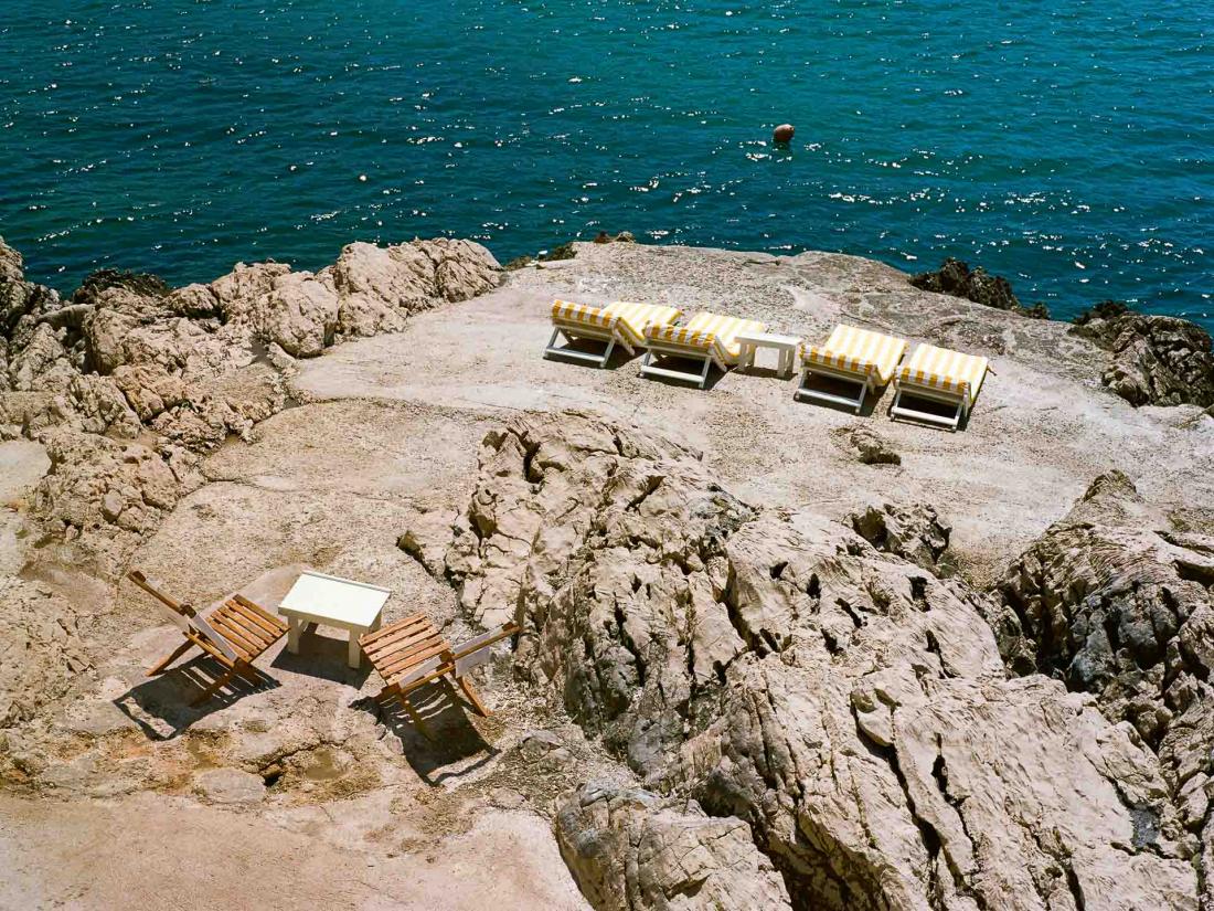 A l’extérieur, matelas aux rayures et tables en bois sur un plage rocheuse