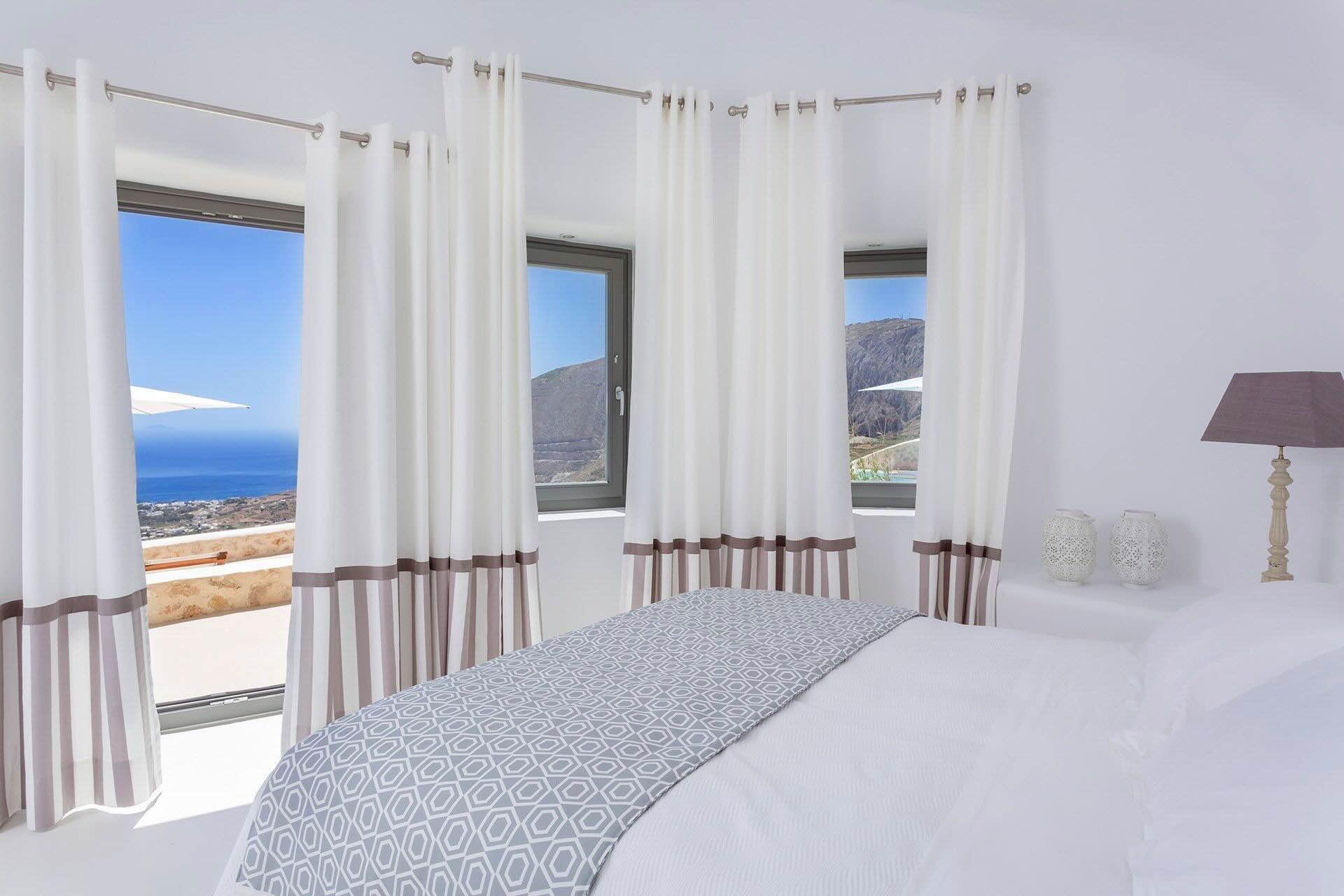 Trois fenêtres, trois panoramas : depuis cette chambre, la vue passe de la mer aux reliefs de Santorin. Le calme de l’intérieur de l’île, dans une villa à louer dans les Cyclades. © Blue Villas