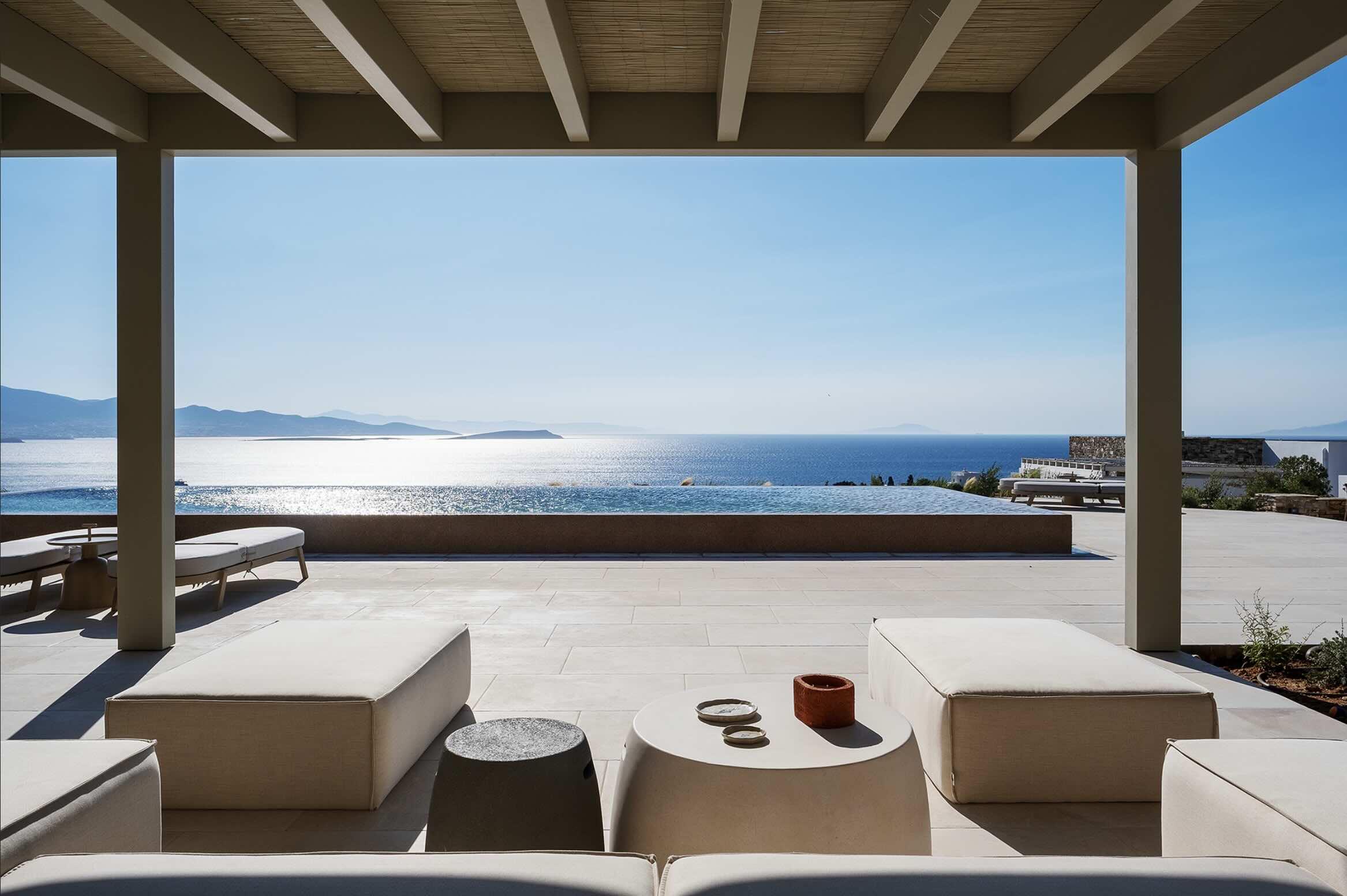 Sous la pergola, le salon d’été fait face à la piscine à débordement et à la mer Égée, avec Paros à l’horizon. Une vue qui résume à elle seule l’attrait de cette villa à louer dans les Cyclades. © Oliaros Villa Rentals