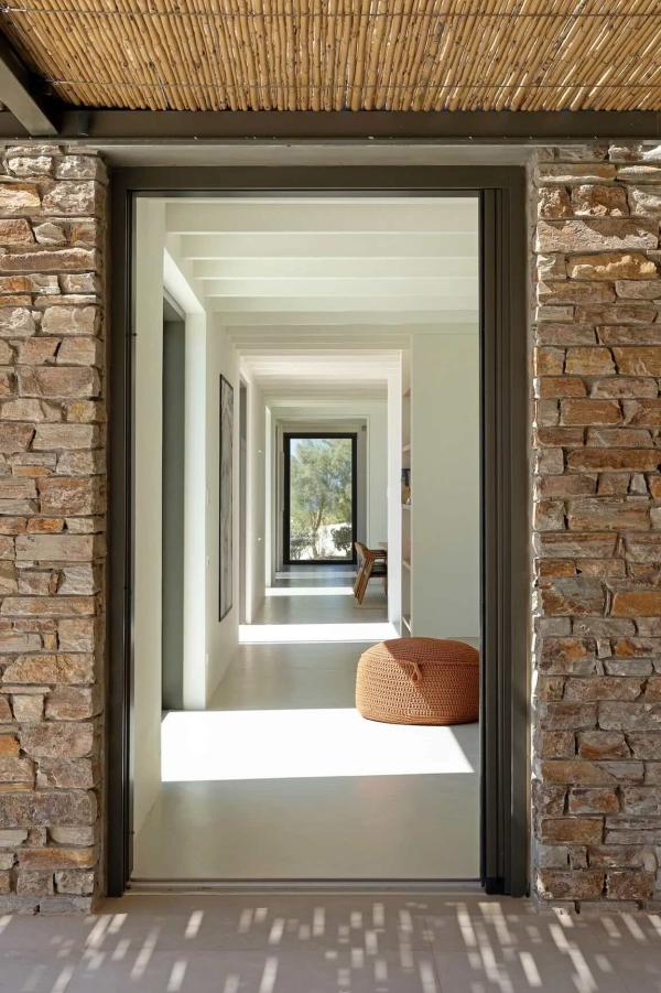 Murs de pierre, canisse et perspective lumineuse : l’entrée de cette villa de luxe dans les Cyclades dévoile une enfilade de volumes blancs. © Le Collectionist