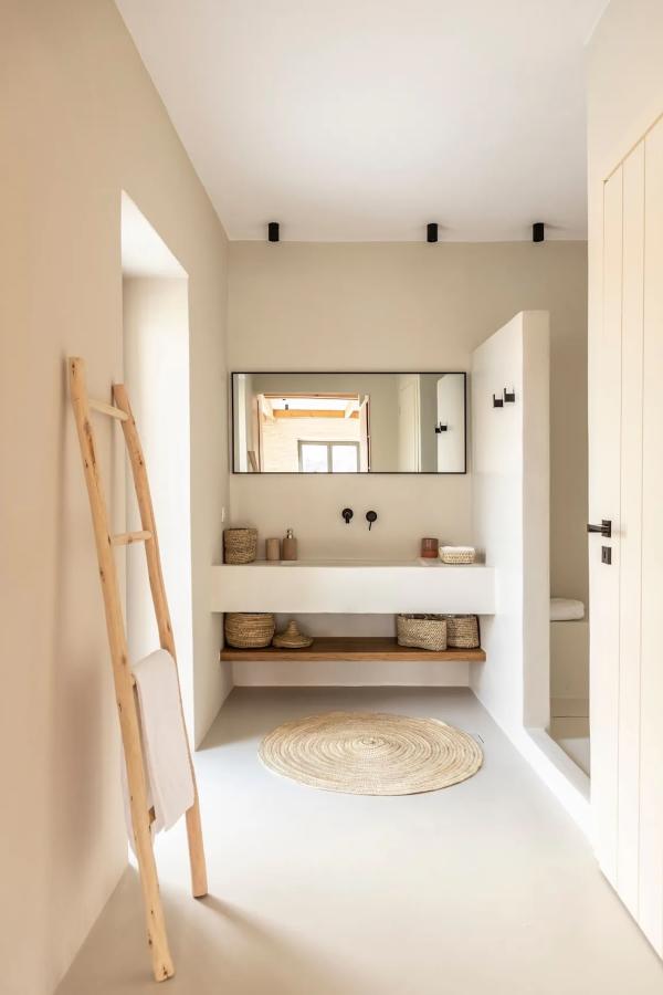 Enduits beige, vasque maçonnée et paniers tressés pour une salle de bains épurée, dans l’esprit de cette villa de luxe des Cyclades. © Le Collectionist